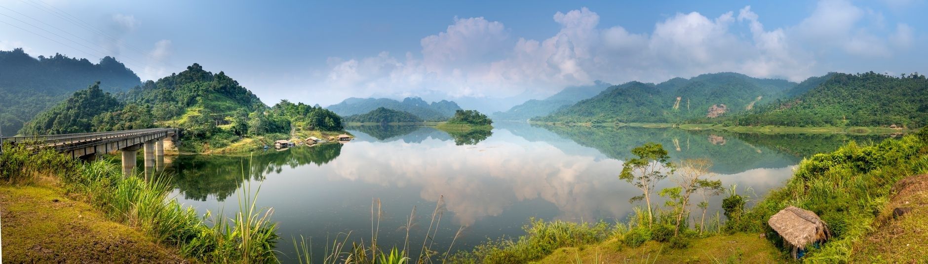 Panoramablick auf See mit Brücke, Ufervegetation und bewaldeten Bergen